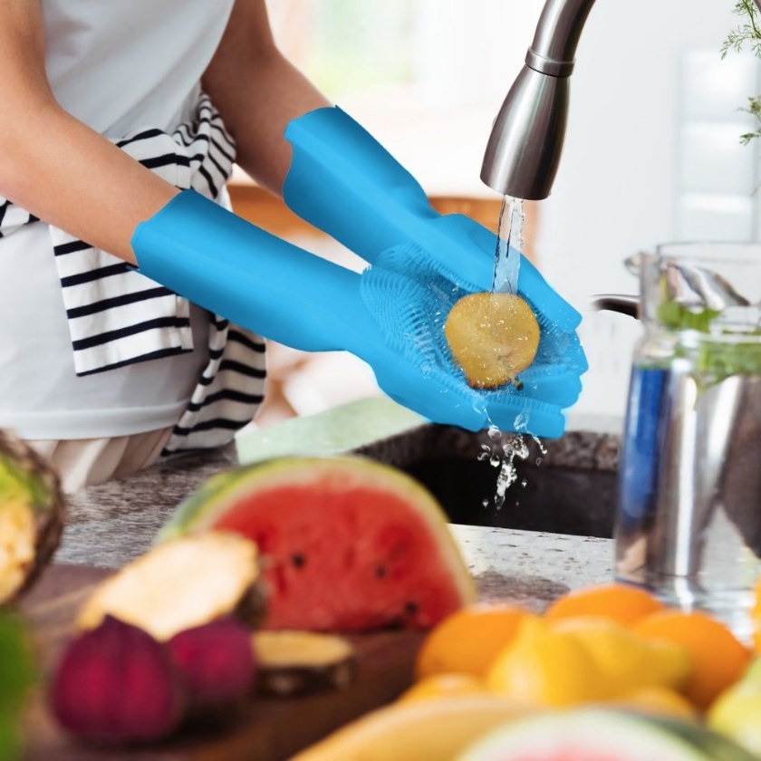 A model wearing a pair of high-temperature resistant, blue dishwashing gloves with scrubbing bristles to wash fruit