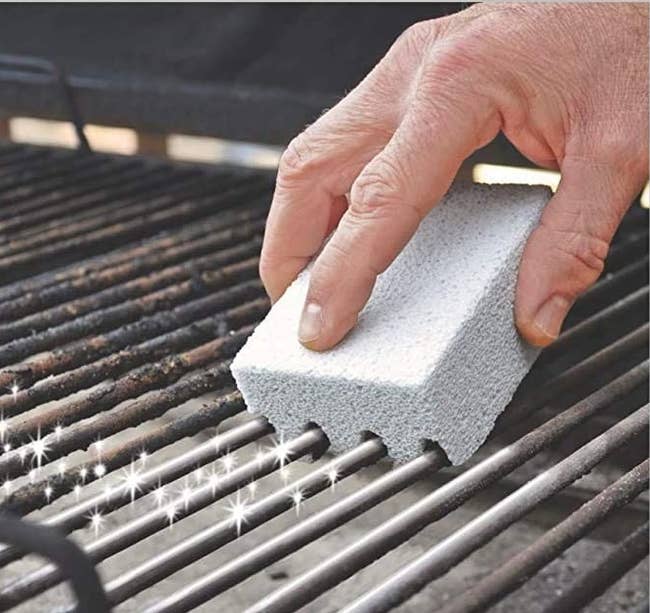 a hand using the scrubber on a dirty grill grate 