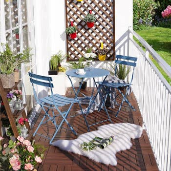 the light blue bistro table and chair set on a small balcony with flowers and plants