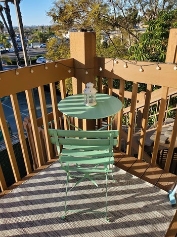 mint green bistro table and chair in the corner of reviewer's studio balcony decorated with string lights