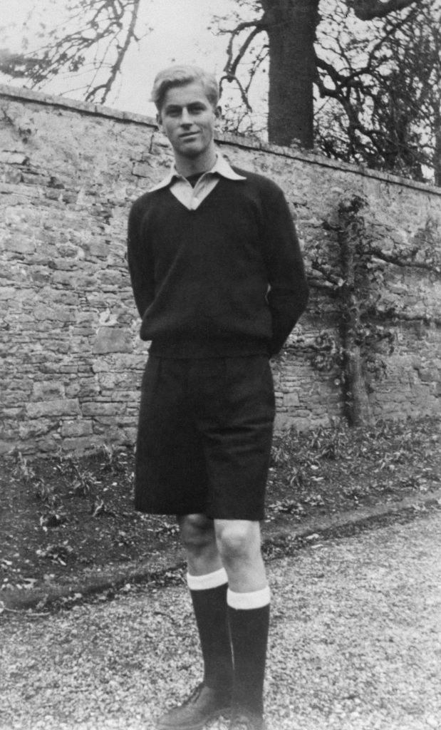 Prince Philip standing outside and wearing a sweater, shorts, and knee-high socks