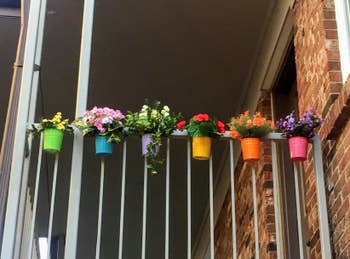 reviewer displays colorful bucket flower pots on their white balcony railing