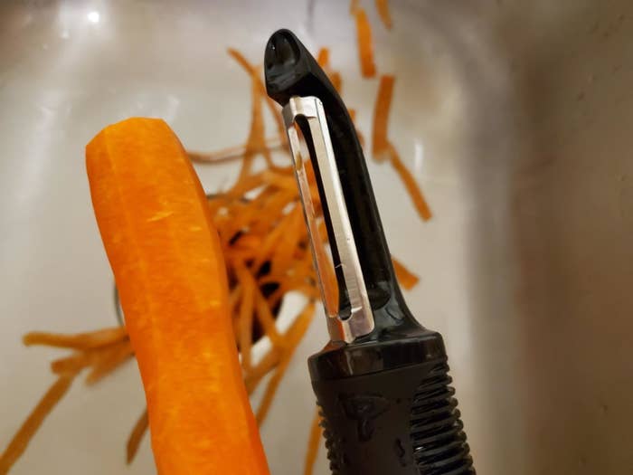 A customer shows off their peeler with a peeled carrot and the peels in the background