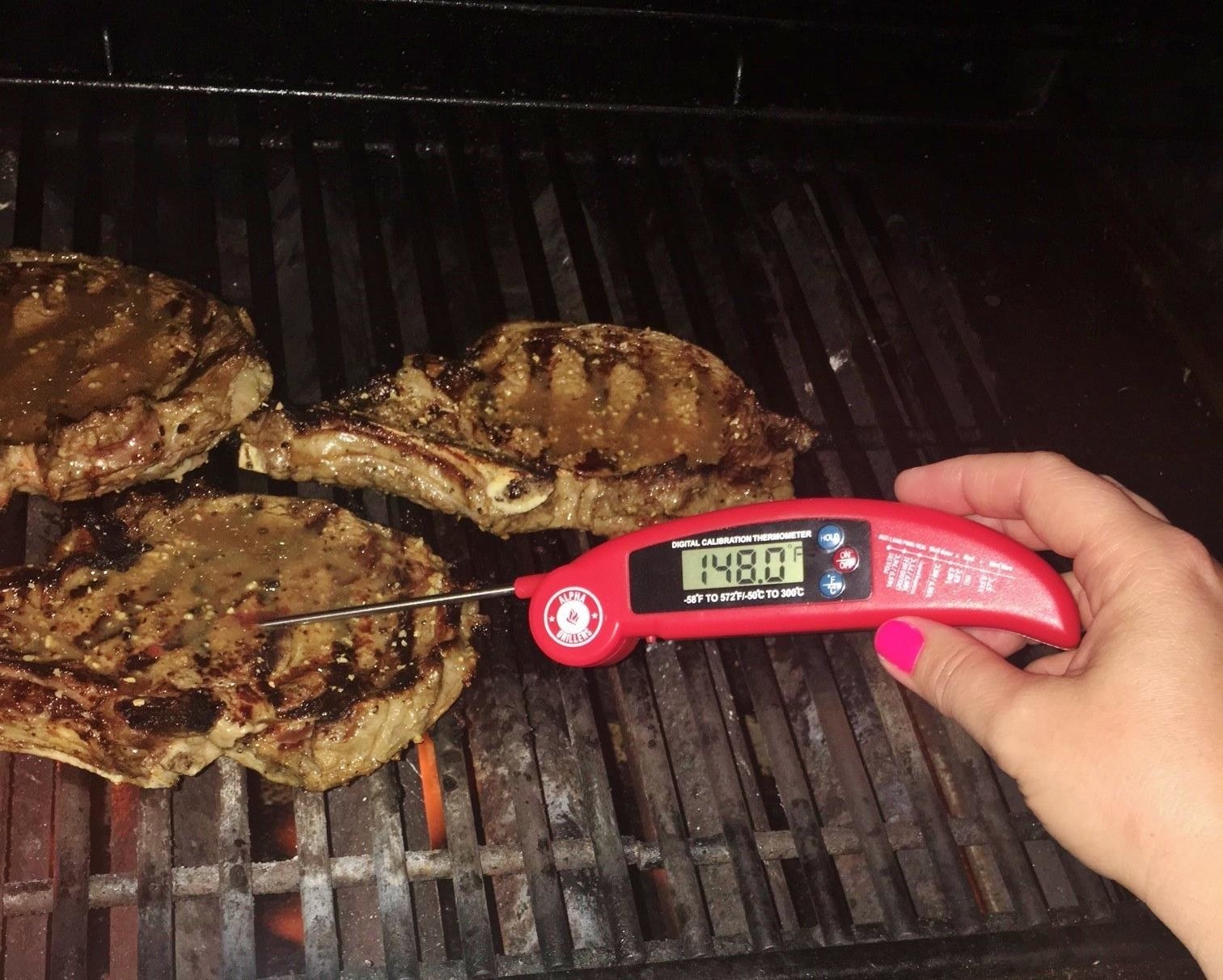A reviewer uses the thermometer in a pork chop on a barbieque