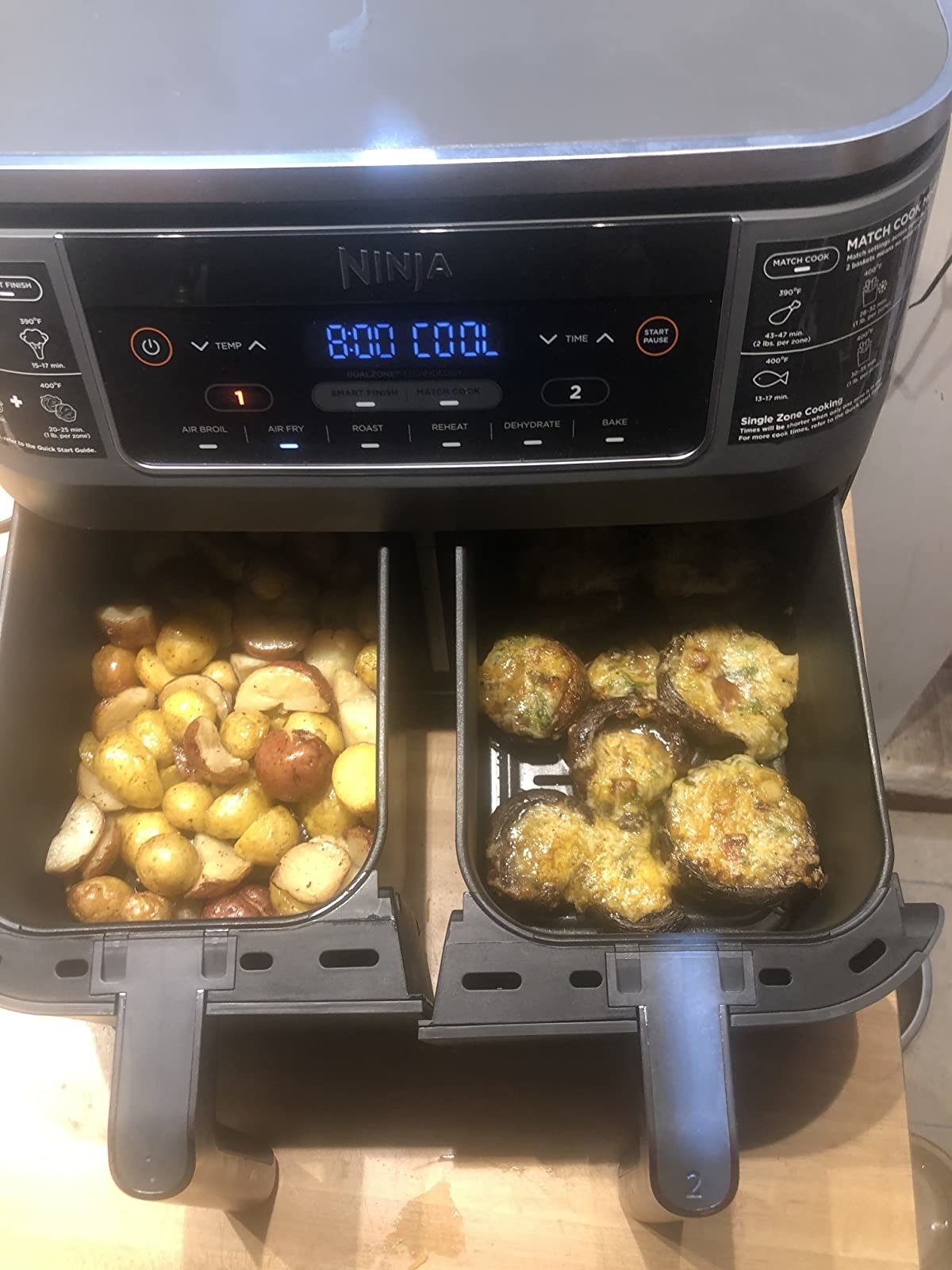 A reviewer has both drawers of the air fryer open, the left with potatoes and the right with stuffed mushrooms