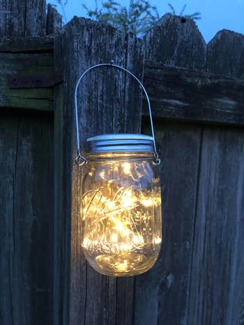 close-up of a mason jar filled with string lights hanging from a fence