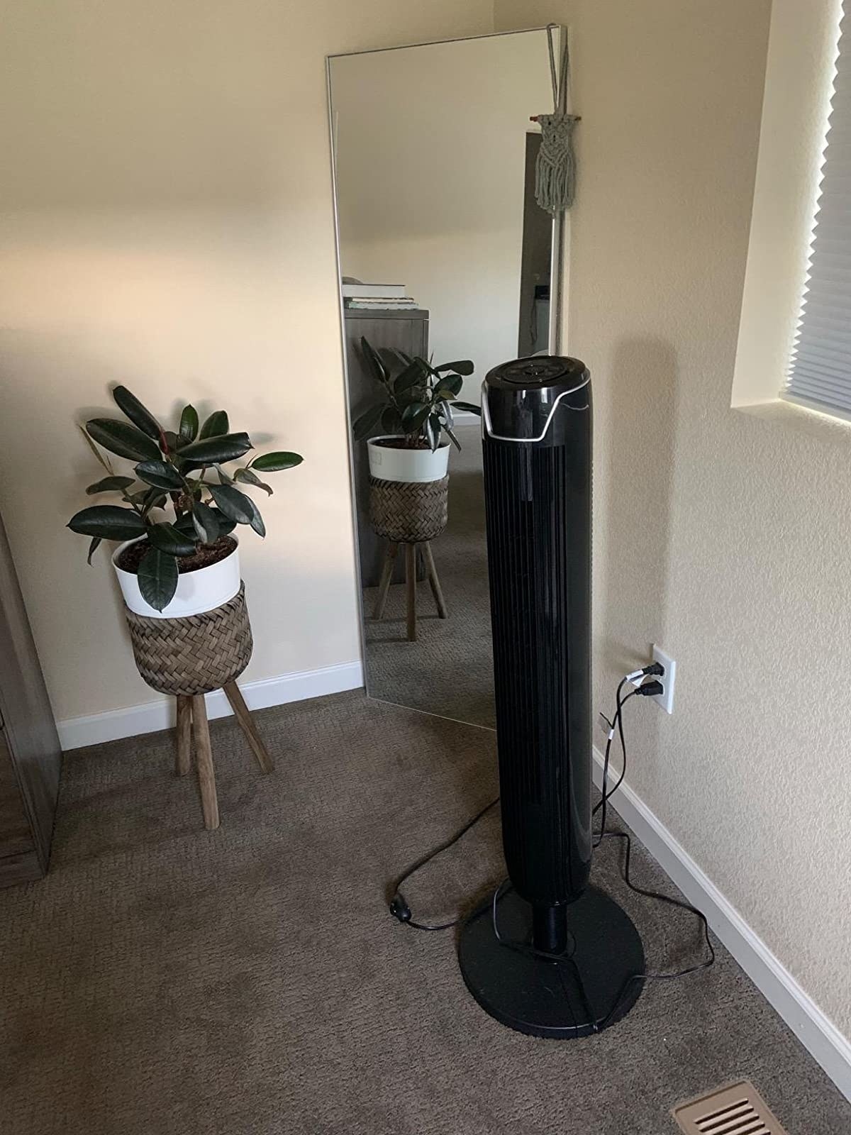 reviewer image of the tower fan in a carpeted living space next to a full length mirror