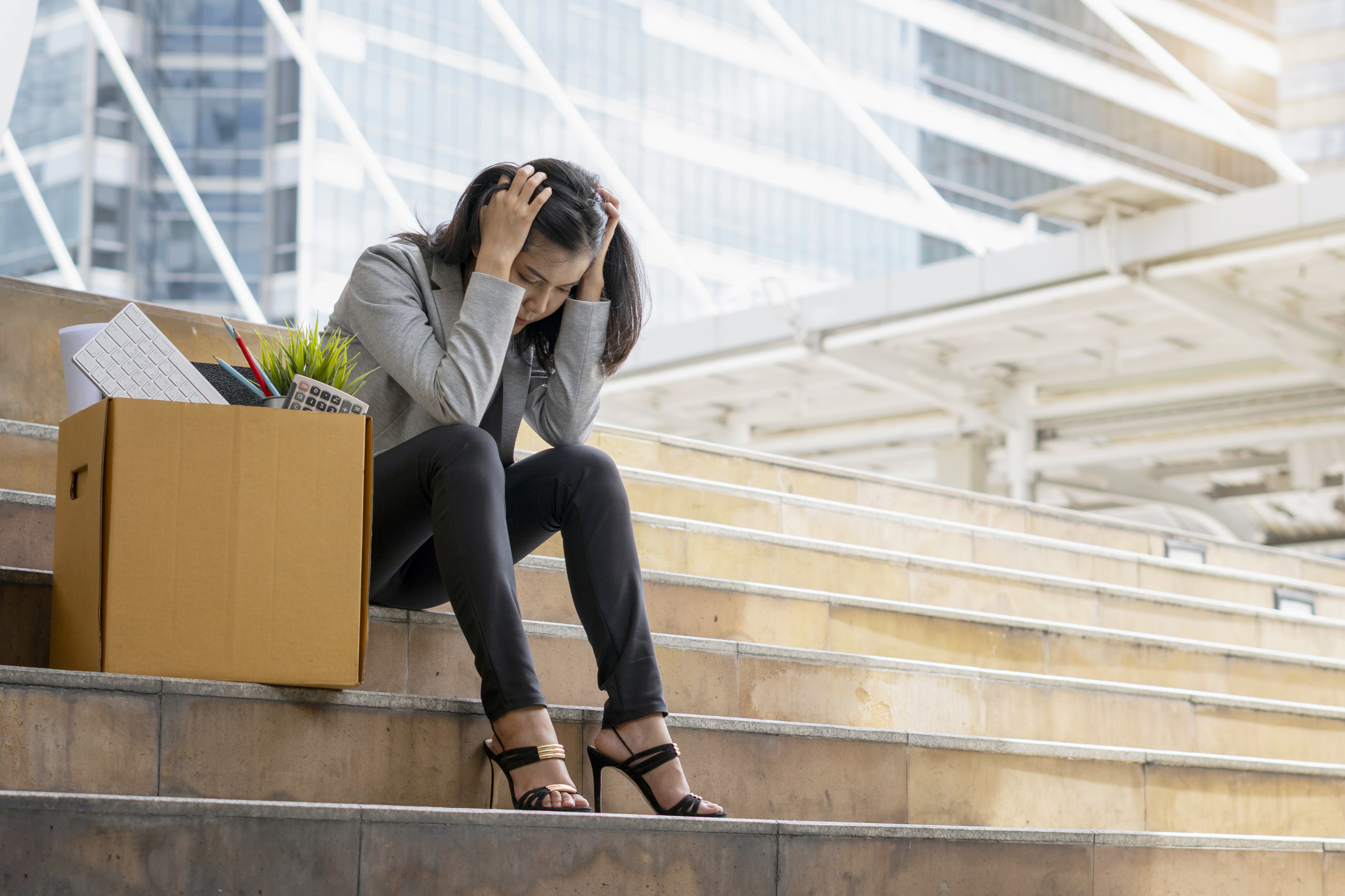 Person who was just fired sitting on steps next to a box of their things