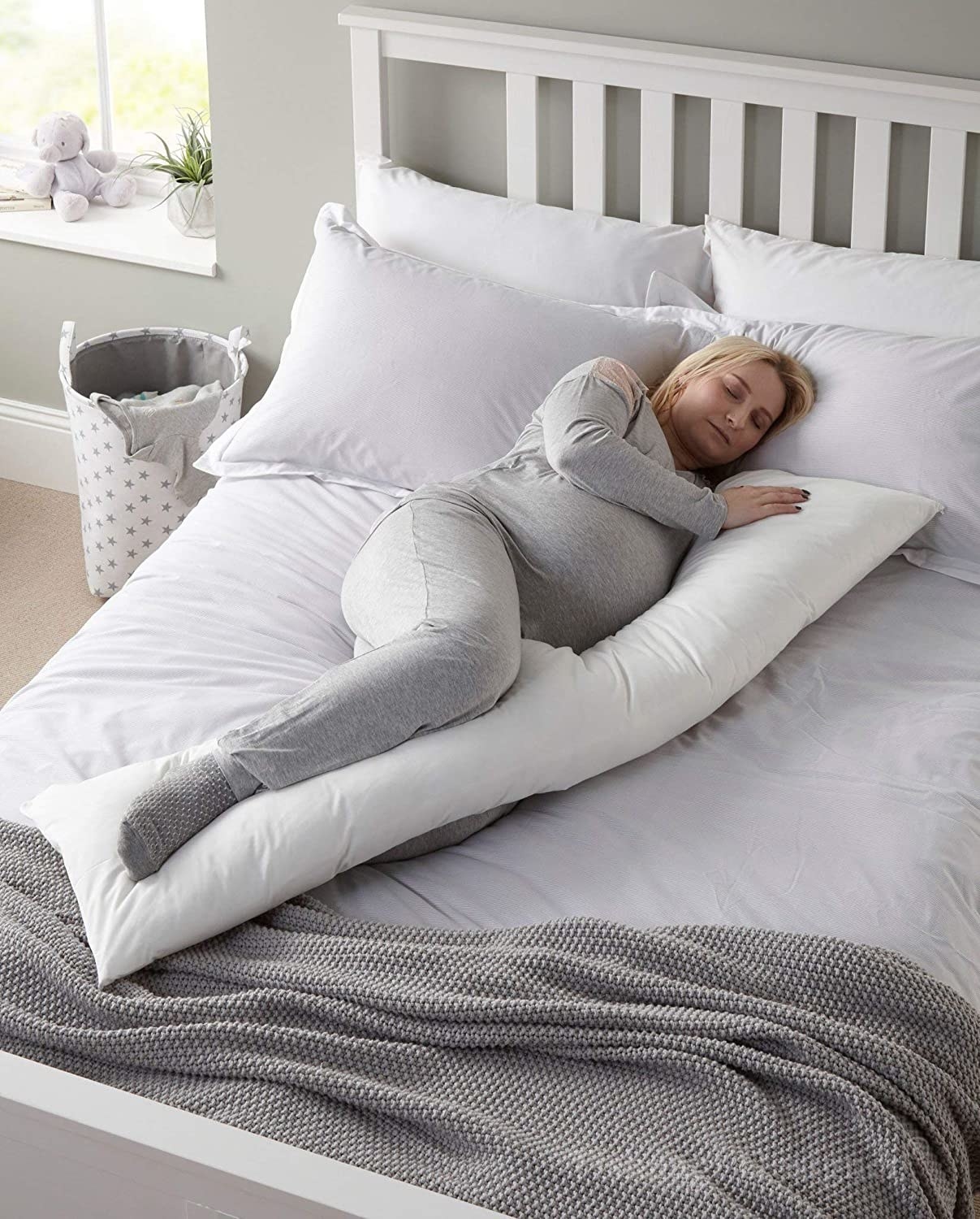 A woman sleeping on her side with a long pillow across her body