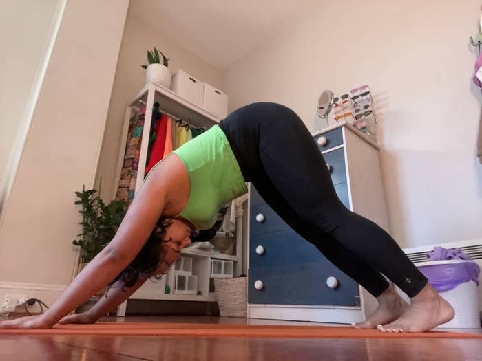 A woman in a green top and black leggings holds a downward dog pose.