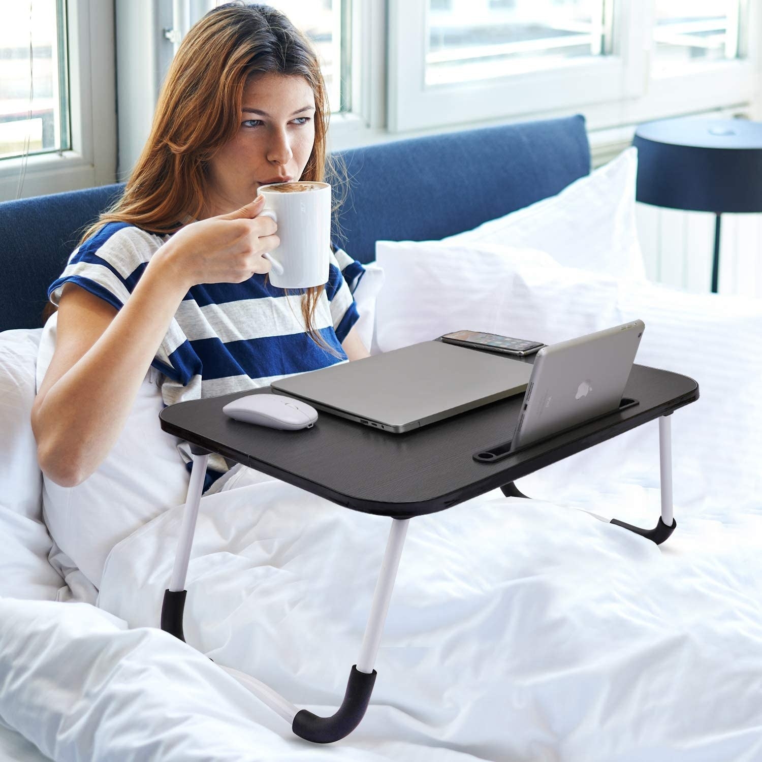 A woman sitting on a bed with the laptop desk.