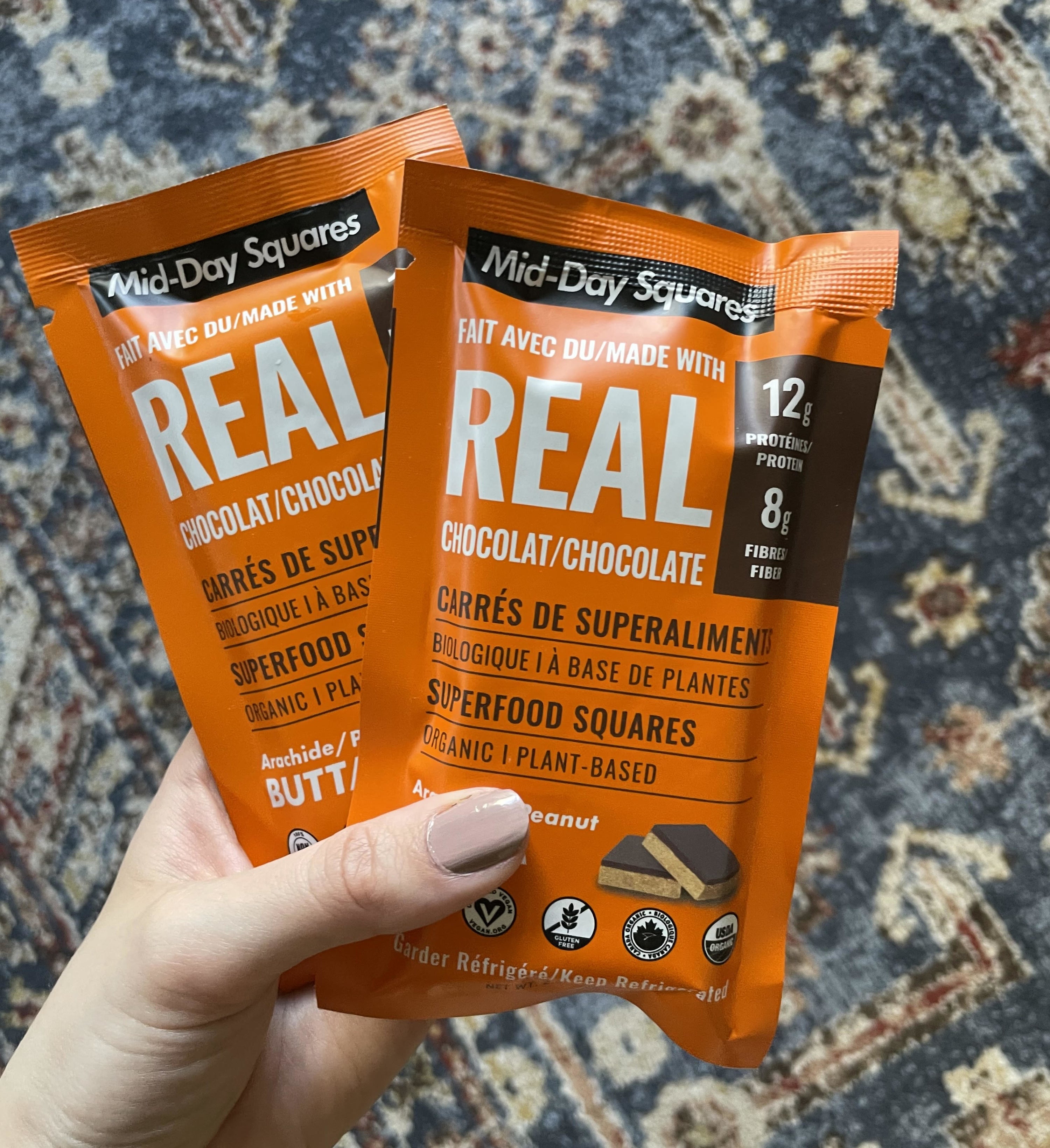 A person holding two packs of Mid-Day Squares