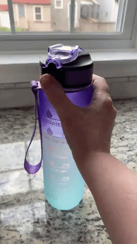 Reviewer popping the lid open to reveal the silicone spout on the purple blue ombre version of the water bottle 
