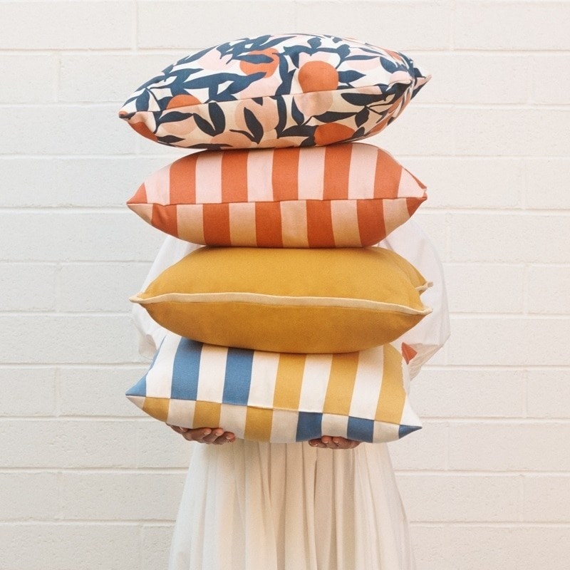 A person holding four vibrant pillows 