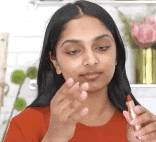 a gif of a model applying red color corrector to their face and then applying foundation 