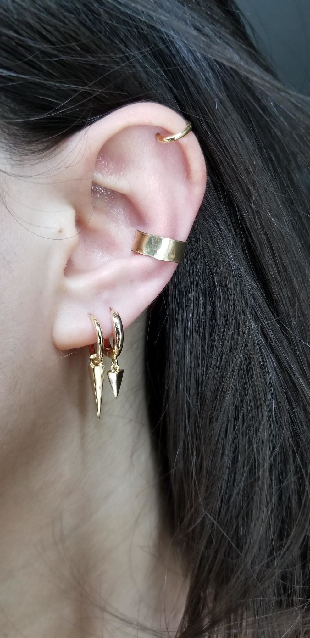 a reviewer wearing two pairs of the gold, arrow-shaped huggie earrings