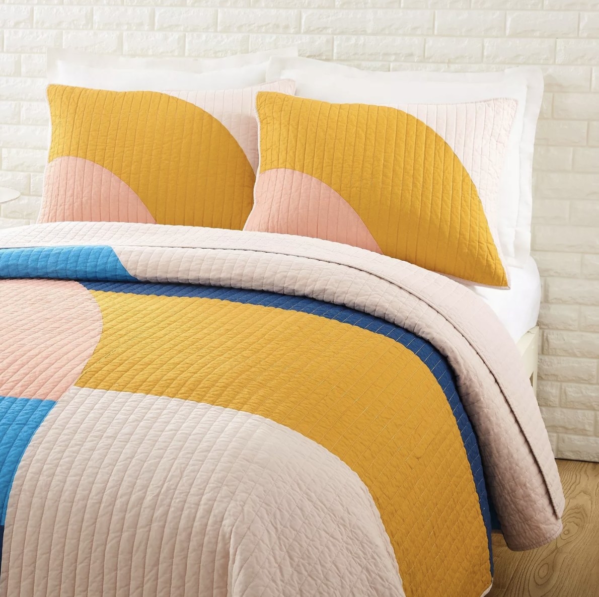 The mod shaped yellow, blue and pink toned comforter on a bed pops in a white room