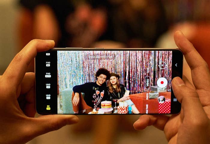 An image of a phone where two people are posing and banners are hung up behind them. 