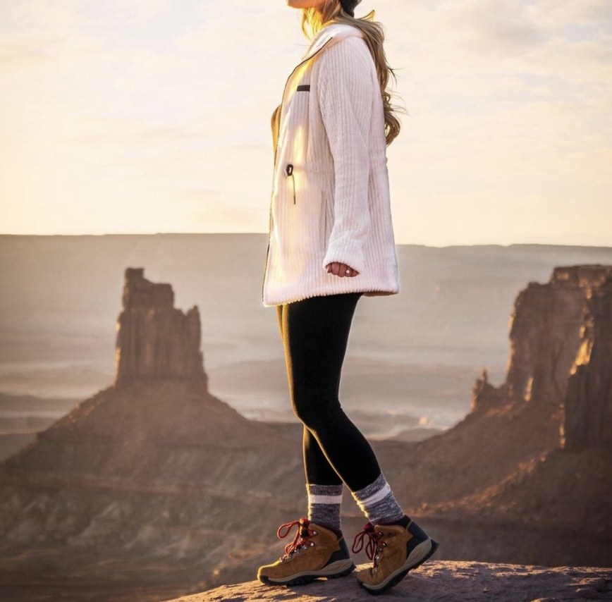 A person on a rock wearing hiking boots, leggings, and a jacket