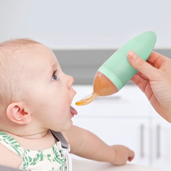 A person feeding their baby with a spoon The spoon has a large tube attached to it filled with baby food