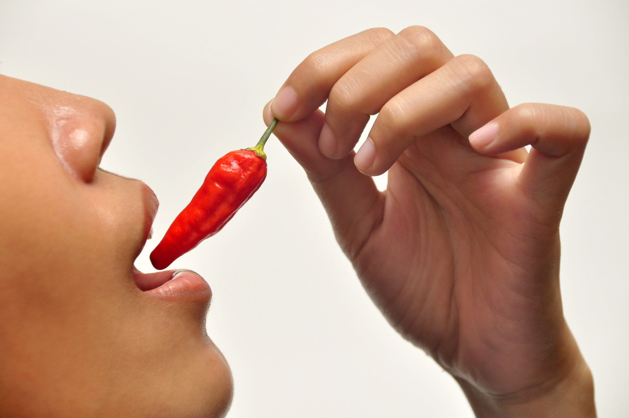 A person putting a spicy hot pepper in their mouth