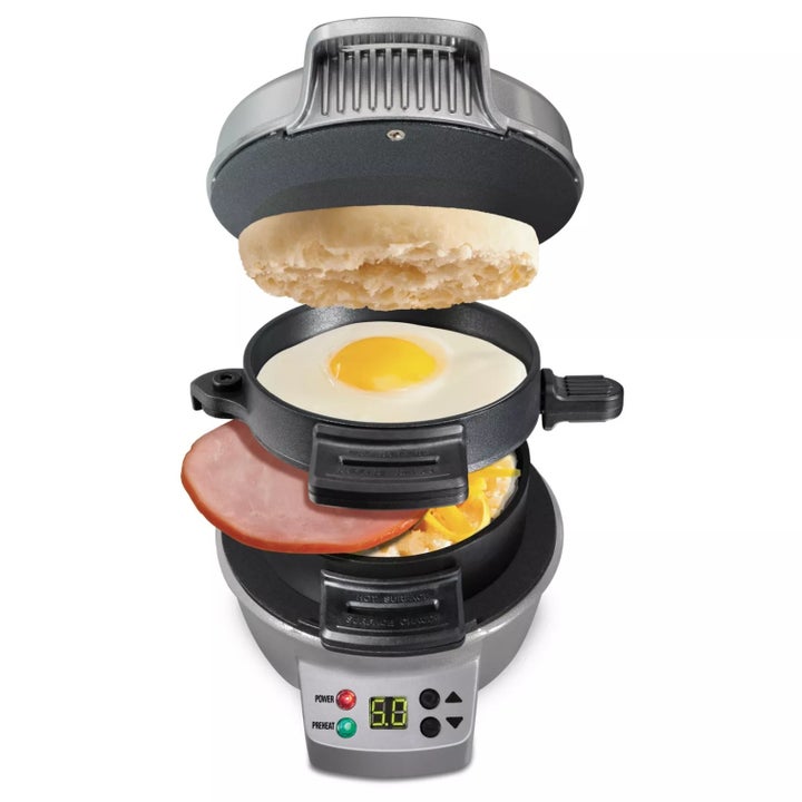 the sandwich maker with an english muffin, egg, ham slice, and cheese in the appliance