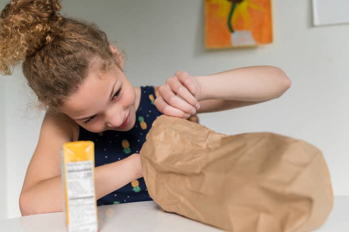A girl looks into a brown paper lunch bag