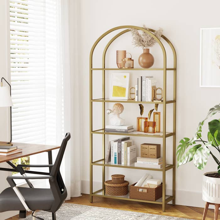 gold arched bookcase displaying various amber, tan, and cream colored decor