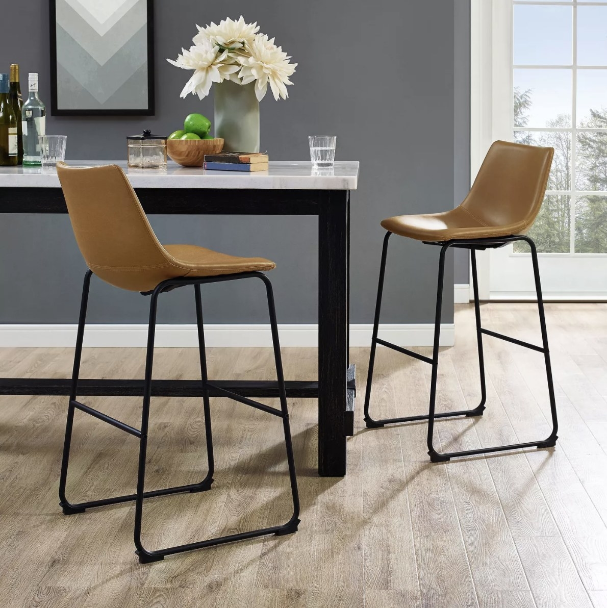 The tan leather barstools are placed around a high marble table with food and drinkware