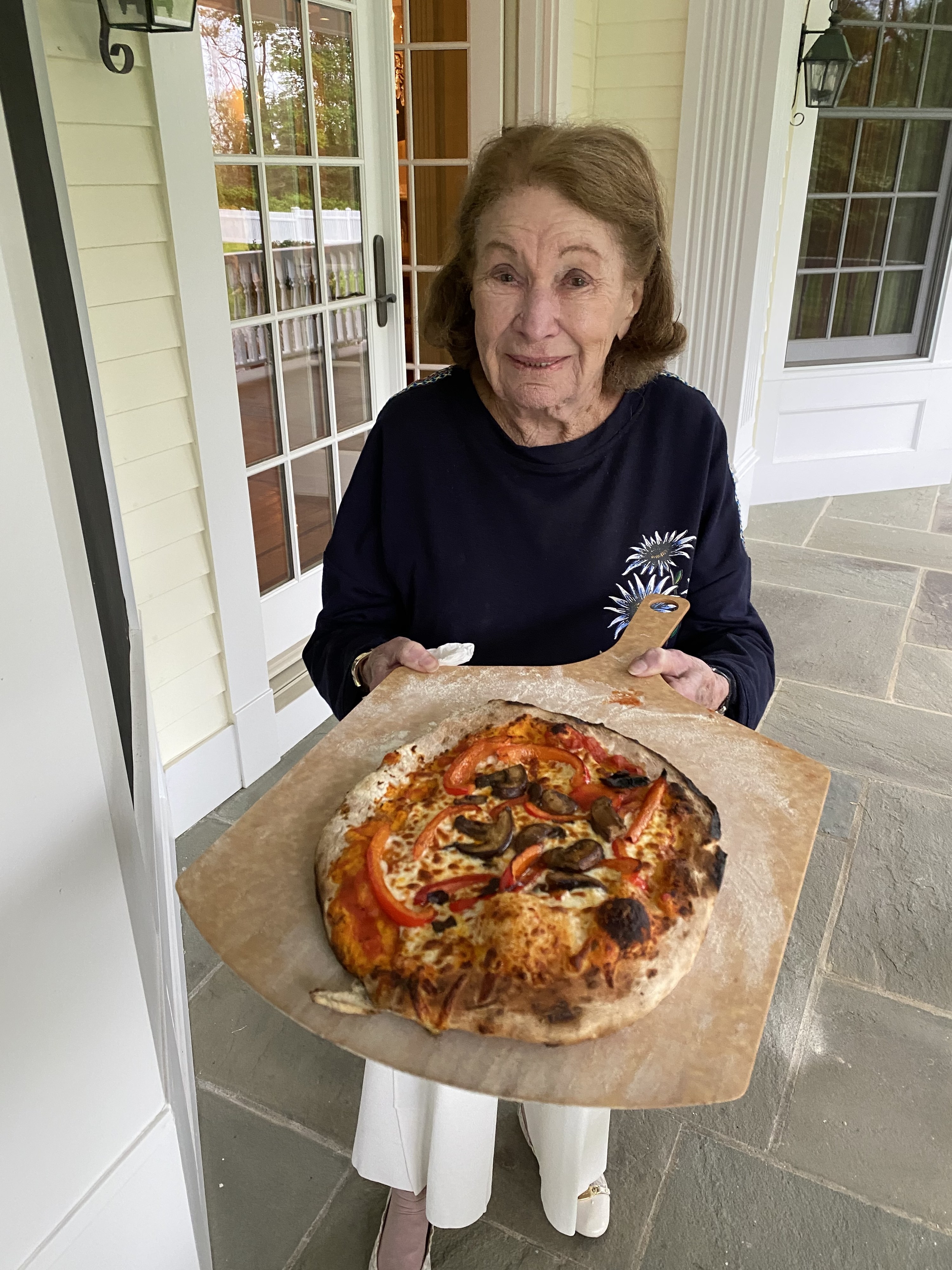 Grandma holding her cooked pizza on a peel and smiling