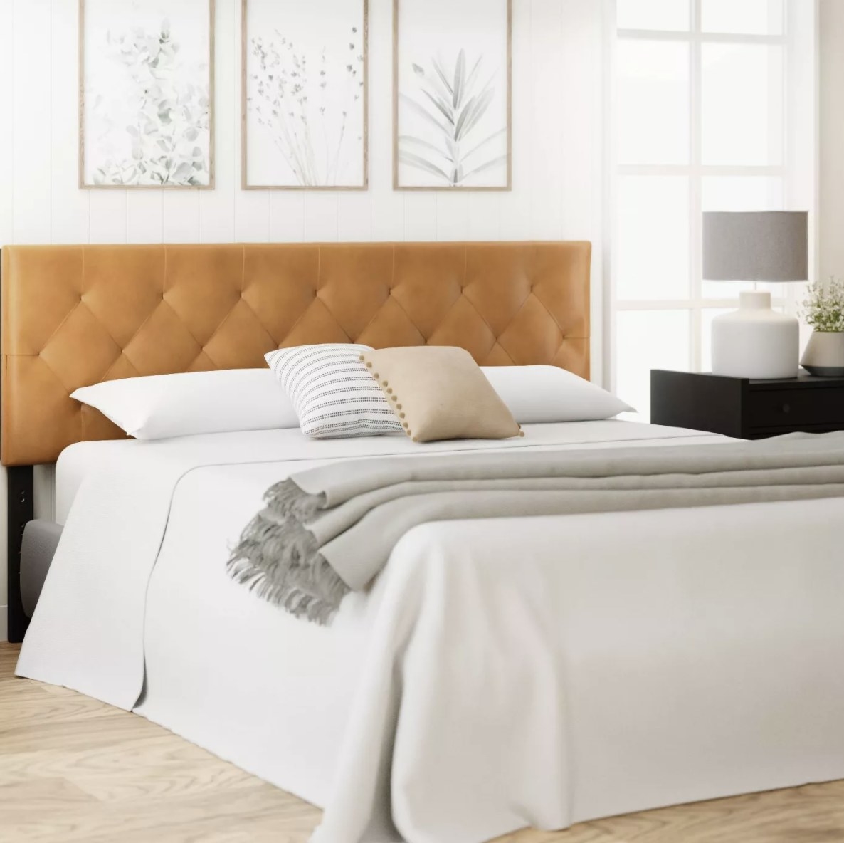The light brown headboard has diamond shapes from the faux leather detailing and pops against a mostly white bed and room