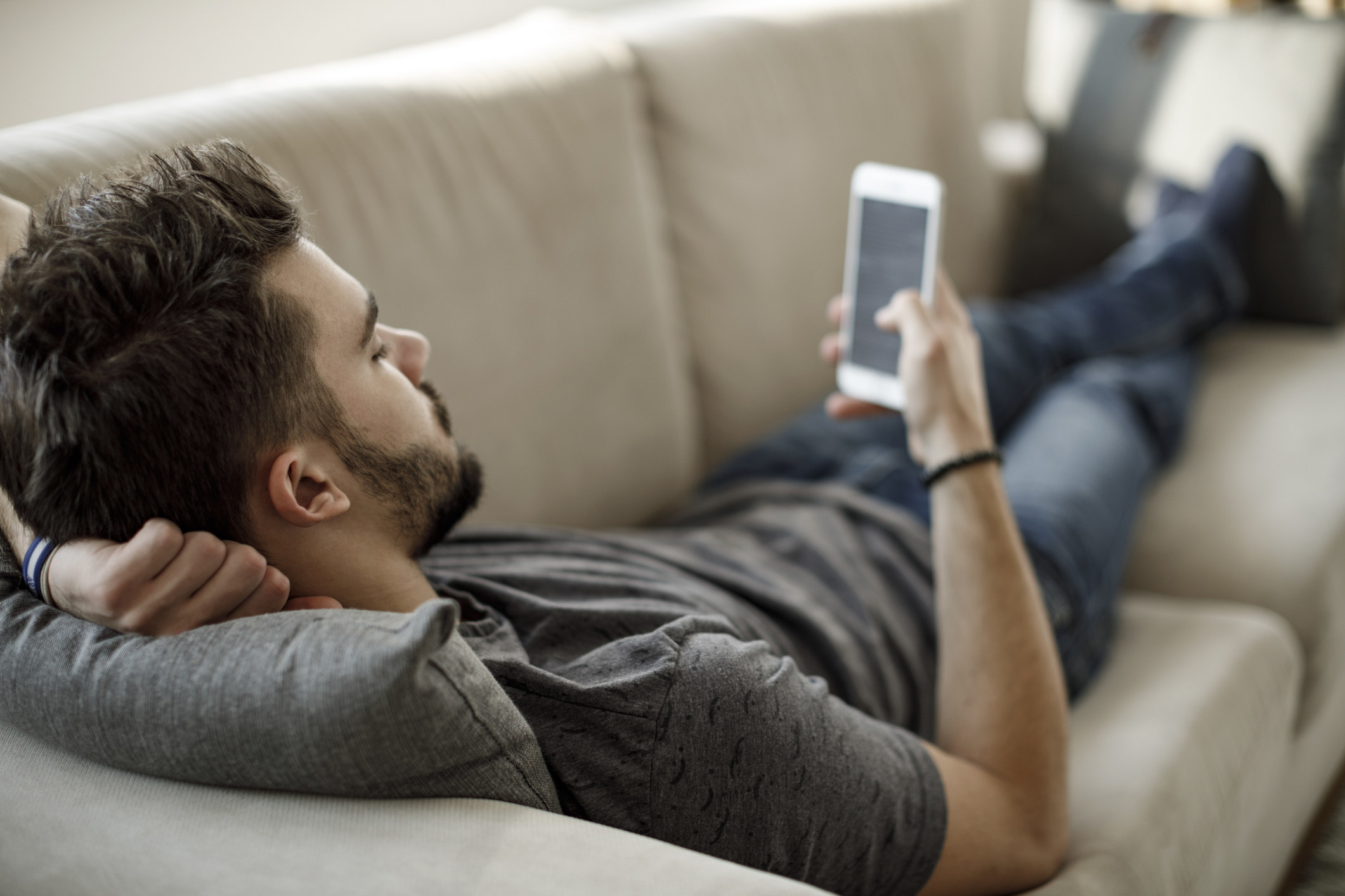 Young man using mobile phone while laying on couch