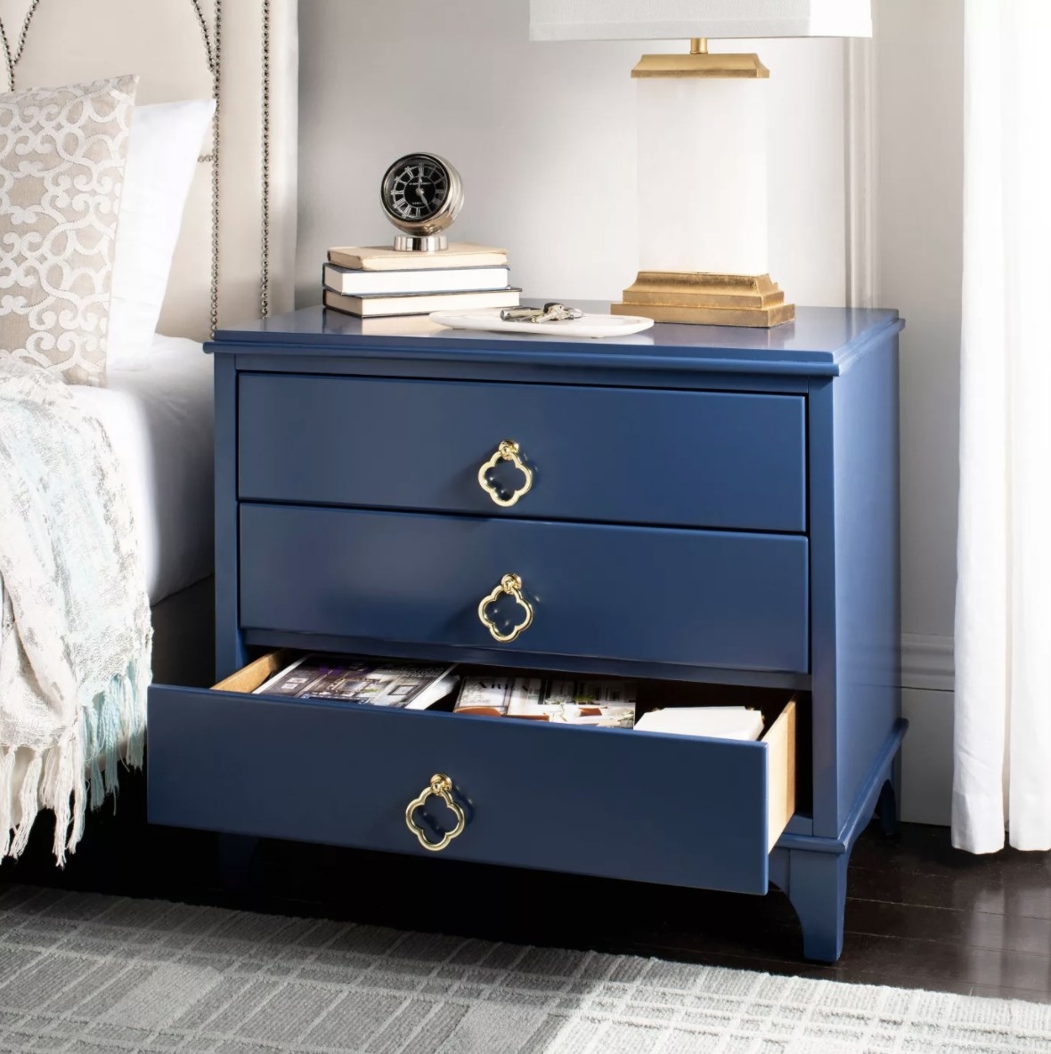 The navy blue dresser has gold handles and one drawer open full of items 