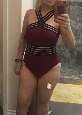 Reviewer in maroon one-piece suit with black stripes at the waist and bust, which has straps with a criss cross design at the chest 