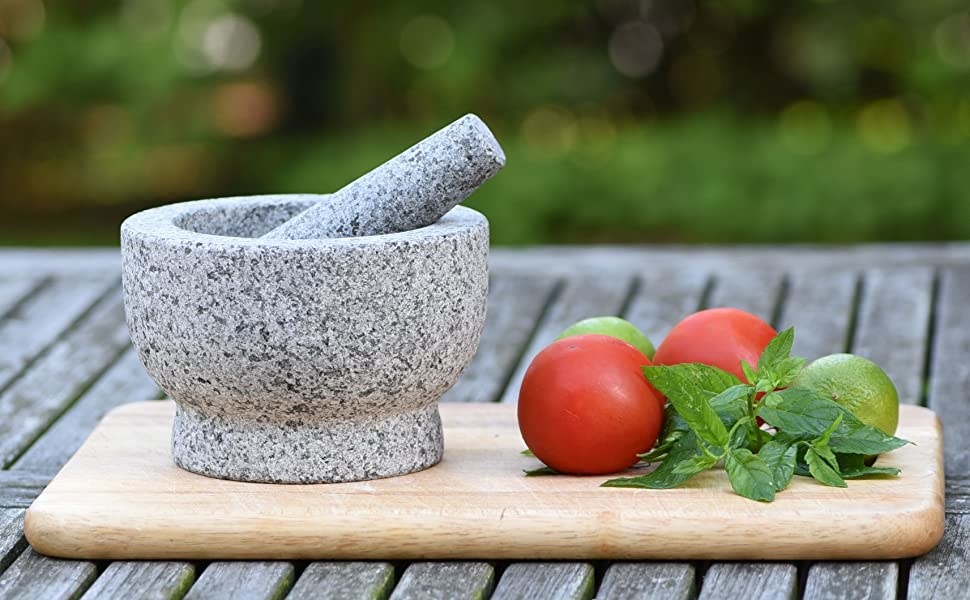 granite mortar and pestle on chopping board with basil, lime, and tomatoes