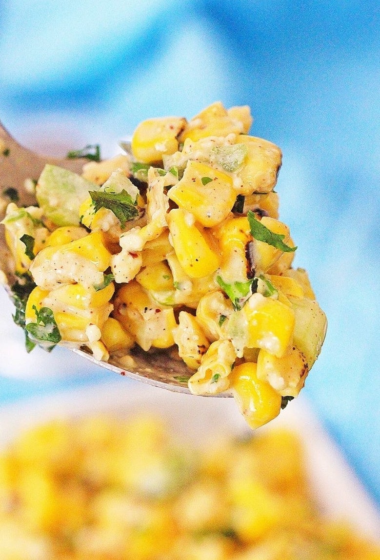 A wooden spoon taking a scoop of Mexican street corn