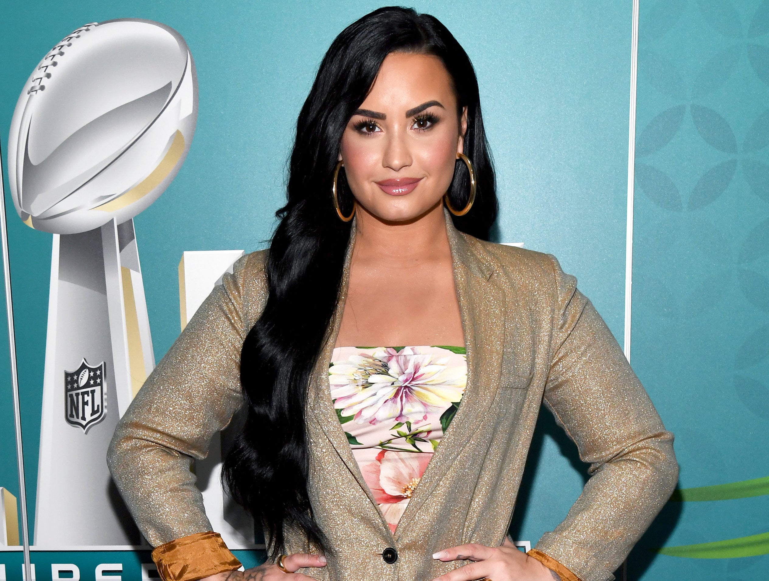 Demi stands with her hands on her hips while wearing a gold blazer