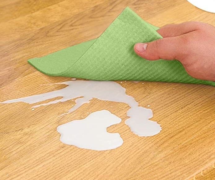 A person cleaning up a spill with one of the biodegradable dishcloths 