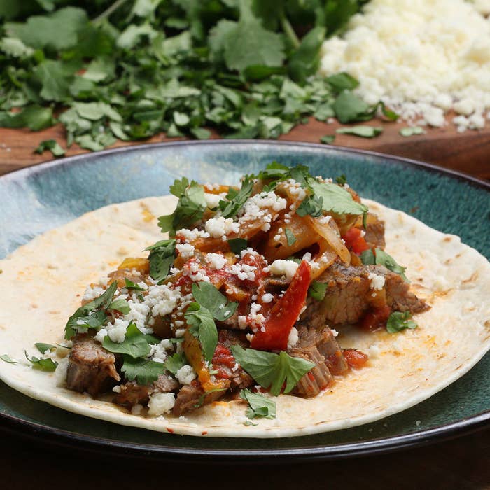 Slow cooker steak fajita in a tortilla with cheese and cilantro.