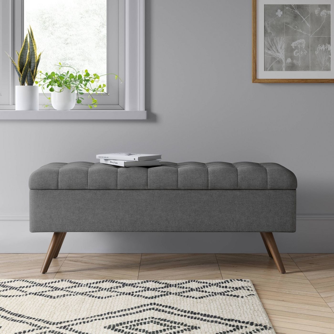 grey upholstered tufted storage bench with books on top