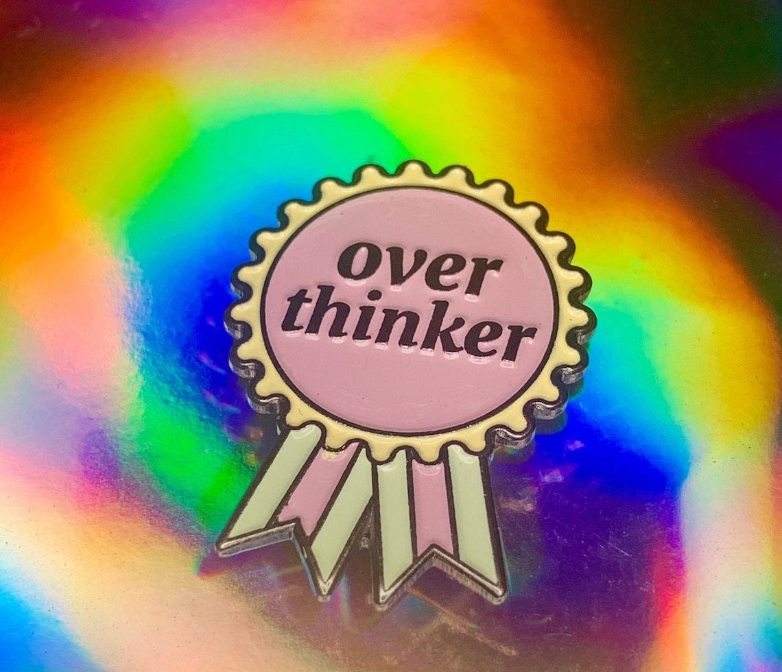 Enamel pin in the shape of a ribbon that says Over Thinker 