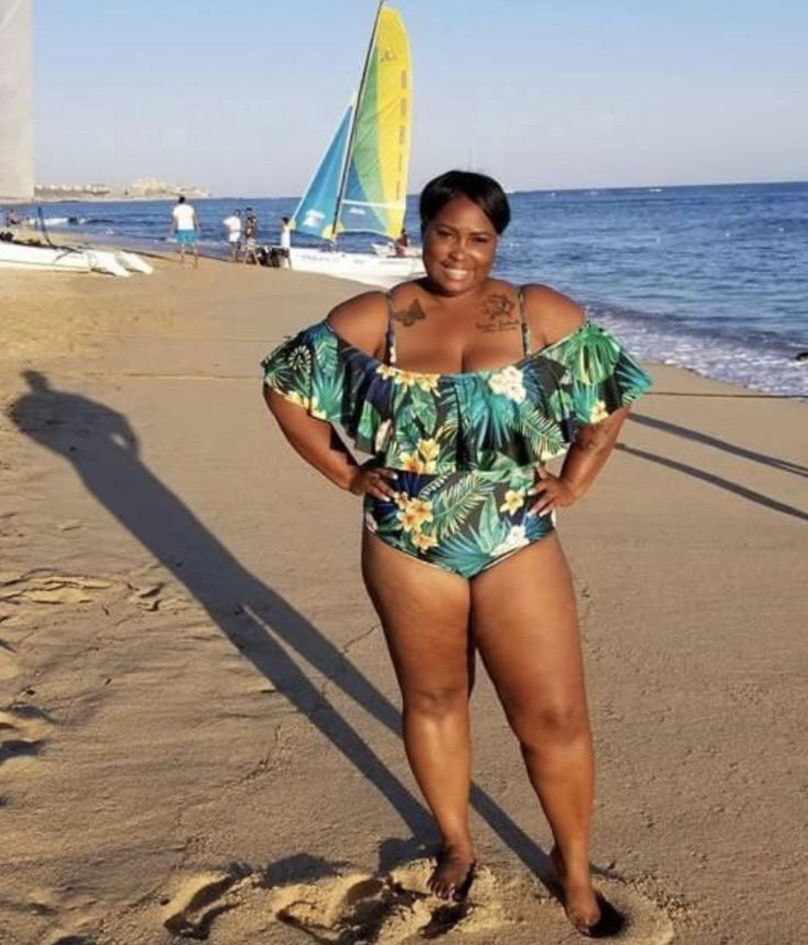 A reviewer wearing the one piece at the beach in the tropical floral print 
