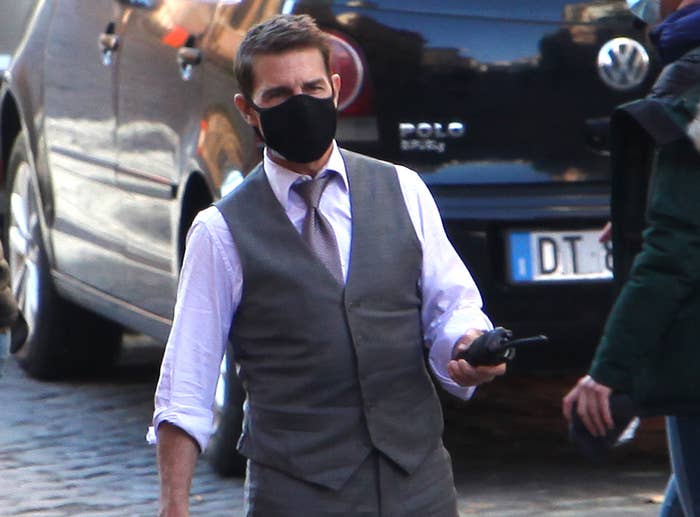 Tom holds a walkie talkie on the set of the movie while wearing a mask