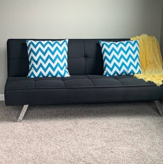 a reviewer&#x27;s black futon with two throw pillows