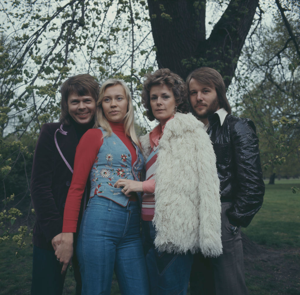 Björn Ulvaeus, Agnetha Fältskog, Anni-Frid Lyngstad, and Benny Andersson posing for a portrait together in a field in the early 1970s