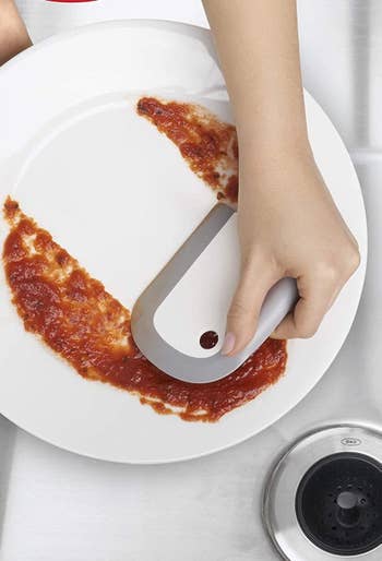 a model hand using the squeegee to get sauce off of a plate 