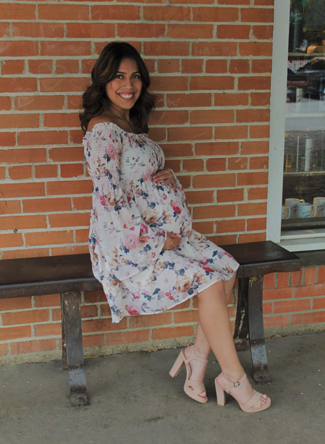pregnant reviewer wearing dress and holding baby while they sit on bench
