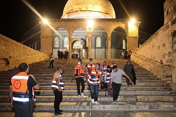 Emergency workers in orange vests carrying injured person down steps of a mosque on a stretcher