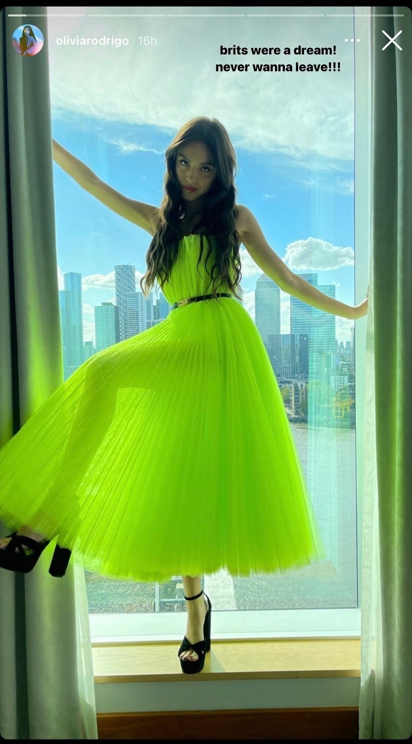 olivia rodrigo in a neon green dress posing in a window on her instagram story