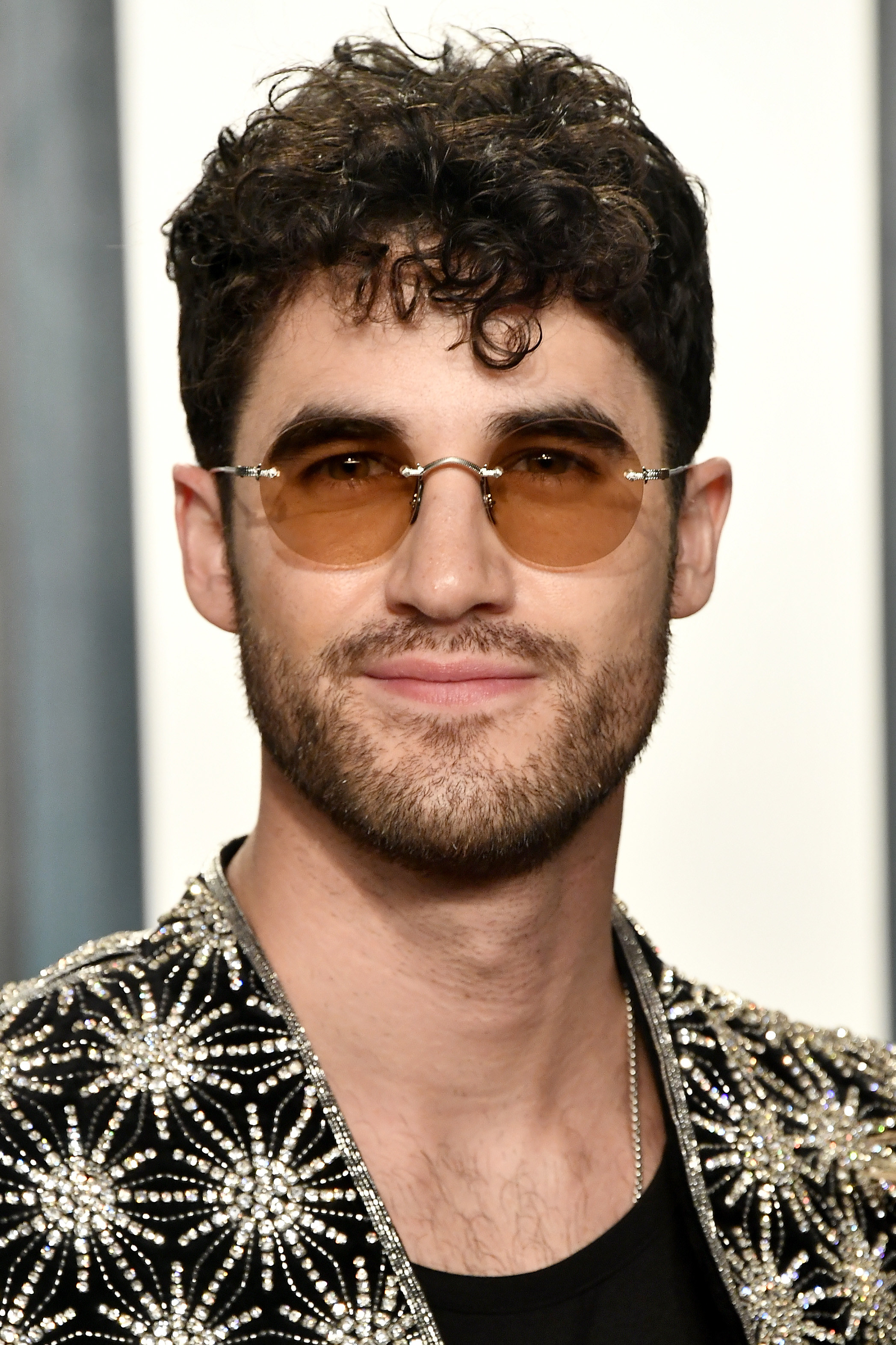 Darren Criss in a beaded blazer and round, brown tinted glasses